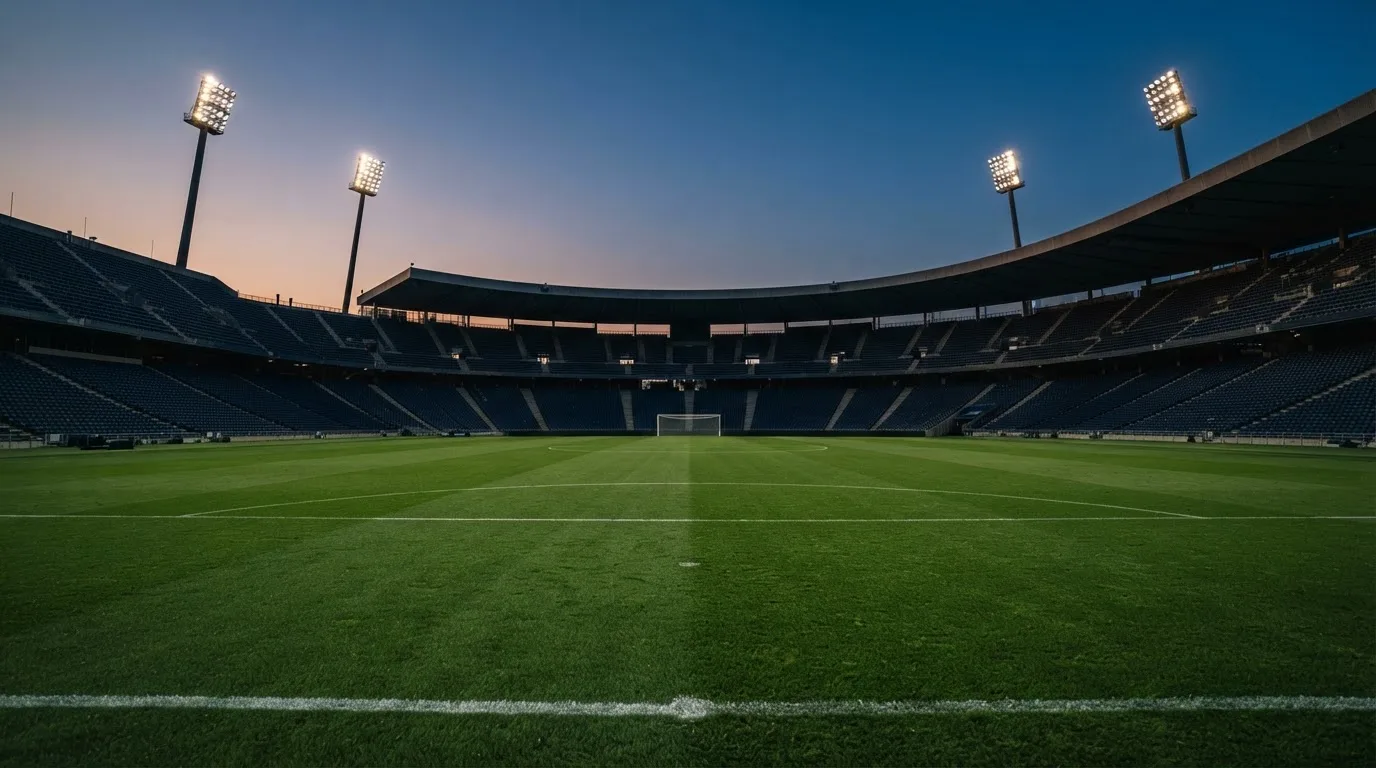 An empty football stadium with floodlight masts at dusk